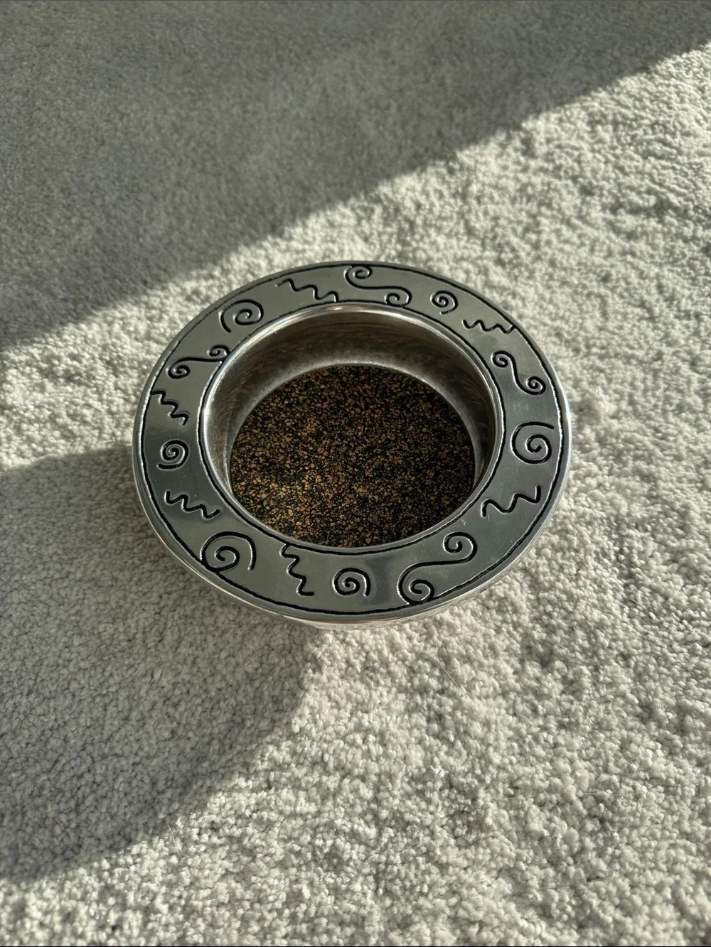 Silver wine bottle coaster with decorative swirl rim.